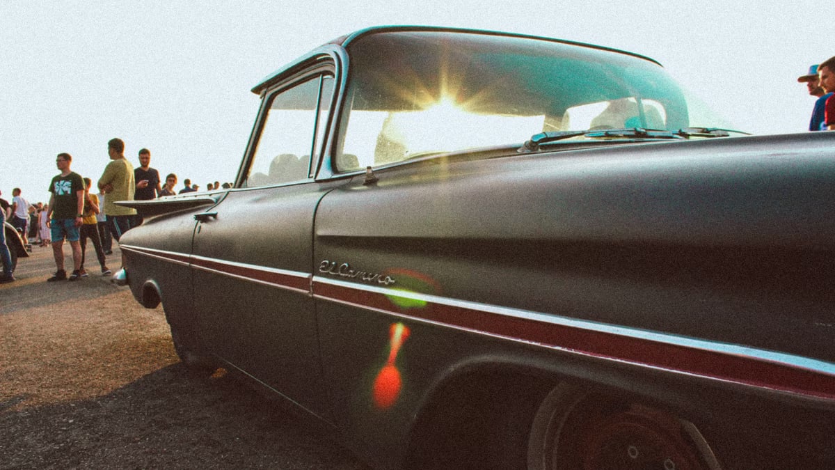 Classic Chevrolet El Camino parked under bright sunlight, surrounded by people at an outdoor event.